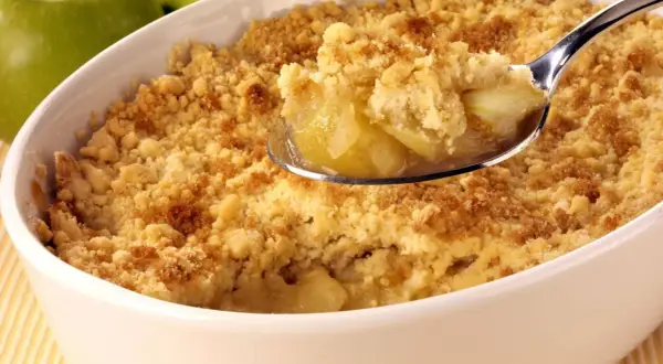Un délicieux crumble aux pommes, parfait pour suivre la recette de Cyril Lignac. La cuillère en argent révèle des morceaux de pommes fondantes sous une pâte croustillante.