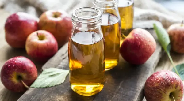 Frische Äpfel umgeben zwei Flaschen mit goldenem Apfelessig. Ein gesundes Elixier, das aus Früchten gewonnen wird.