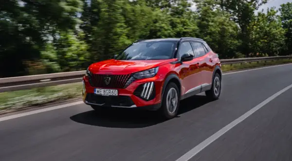 Czerwony Peugeot 2008 GT pędzi po drodze, otoczony zielenią drzew.