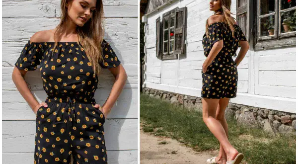 Krótki kombinezon hiszpanka w słoneczniki, idealny na letnie dni. Modelka prezentuje go na tle drewnianej chatki.