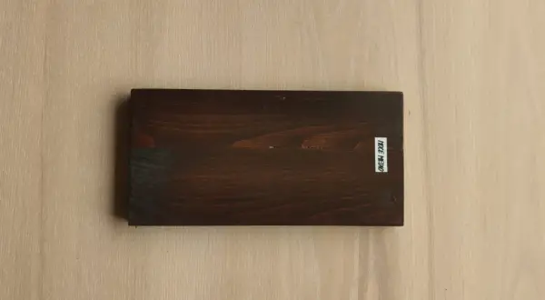 Tavola scura con evidenti venature del legno, su sfondo chiaro con venature simili. Etichetta bianca con scritta "NOCE MEDIO".