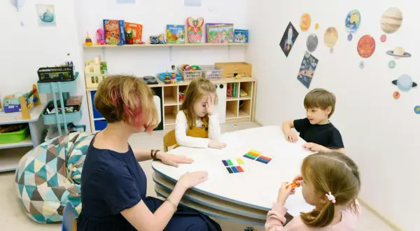 Ergotherapie Teilzeit Ausbildung: Kinder malen und basteln mit einer Therapeutin in einem bunten Raum.