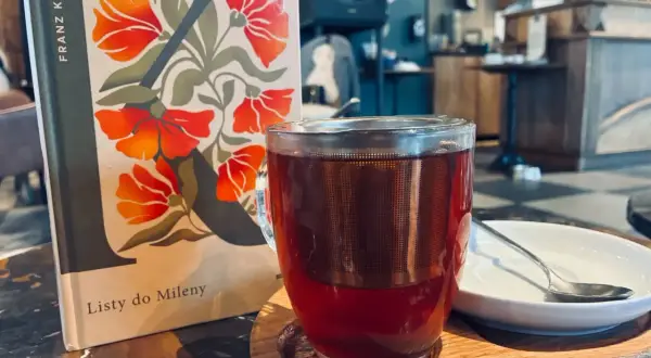 Kawa i książka "Listy do Mileny" Franza Kafki na stoliku w kawiarni.