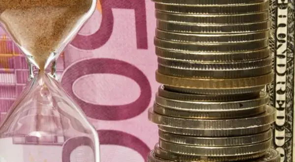 Klepsydra i stos monet na tle banknotu 500 euro. Czy numizmaty co to, to tylko monety?