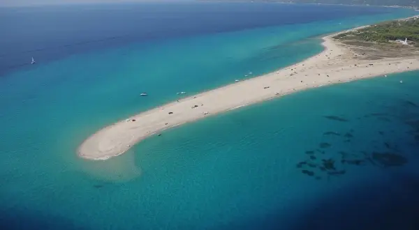 Plaża na Chalkidiki, przypominająca język lądu wcinający się w turkusowe morze. W oddali widać wybrzeże i budynki, może nawet lotnisko.