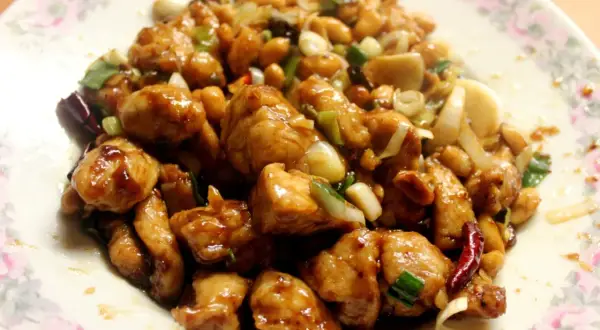 Kurczak Gong Bao z orzeszkami ziemnymi, cebulą i papryczkami chili na talerzu.