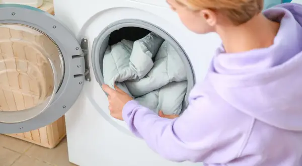 Frau legt eine Daunenjacke in die Waschmaschine. So wird die Daunenjacke gewaschen.
