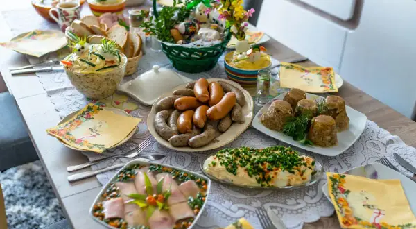 Obficie zastawiony stół z wieloma potrawami, w tym kiełbasami, galaretą i sałatkami. To idealne przystawki na Wielkanoc.