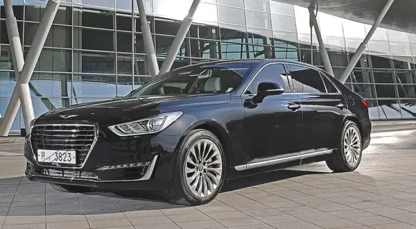 Elegancki, czarny Genesis G90 lśni przed nowoczesnym budynkiem.