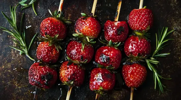 Zuckersüße Erdbeeren auf Spießen, leicht gegrillt und glänzend, mit Rosmarin garniert. Ein Genuss für alle Sinne!