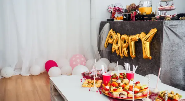 Złote balony z napisem "PARTY" i przekąski na stole tworzą atmosferę wieczoru panieńskiego w domu.