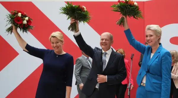 Uśmiechnięta Astrid Ann Marie Pollmann i politycy z bukietami kwiatów na tle czerwono-białej ściany.