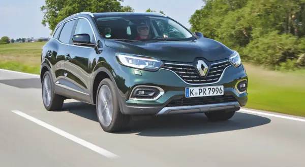 Zielony Renault Kadjar jedzie po drodze, za kierownicą mężczyzna w okularach.