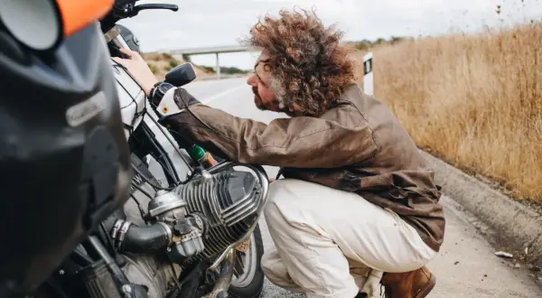 Hombre con pelo rizado revisa su moto 125, preguntándose cuanto aire lleva.
