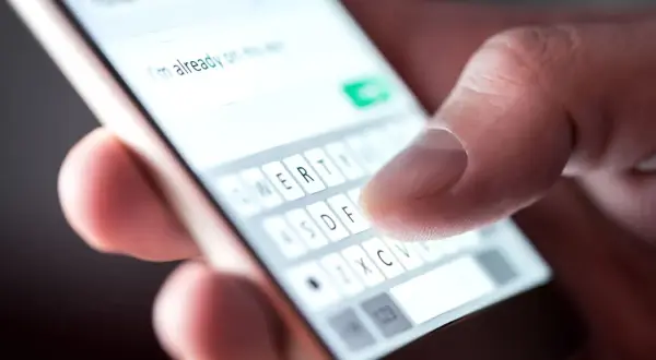 Palec pisze na klawiaturze telefonu: "Już w drodze". Potwierdzenie przybycia na wesele sms.