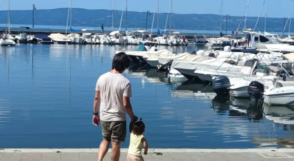 Padre e figlia passeggiano sul lungolago di Bolsena, con barche ormeggiate sullo sfondo.