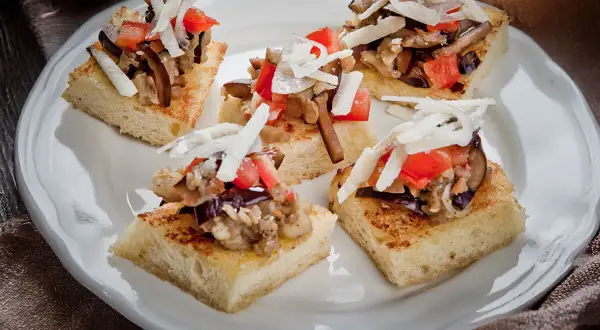 Deliziosi crostini con melanzane, pomodoro e scaglie di formaggio su pane tostato.