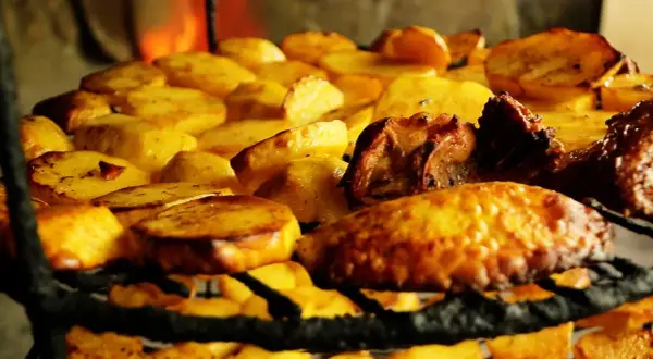 Patatas asadas y carne sobre una parrilla, un delicioso plato de comida típica de Armenia, con fuego al fondo.