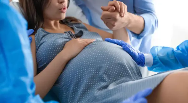Mujer dando a luz en un parto natural, apoyada por su pareja y personal médico.