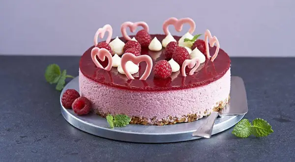 En vacker hallonmousse tårta med färska hallon och rosa hjärtdekorationer, perfekt för ett speciellt tillfälle.