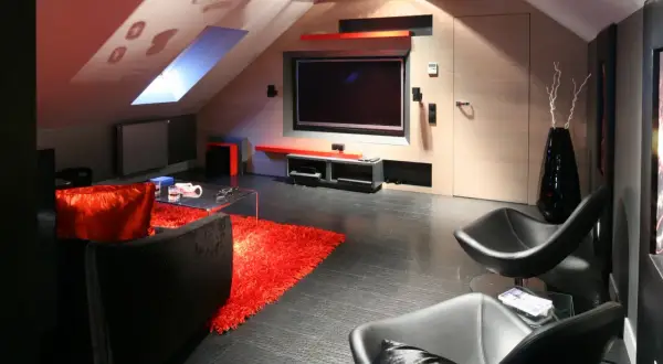 Nowoczesny salon na poddaszu ze skosami. Telewizor zamontowany na ścianie, obok wygodne fotele i kanapa.
