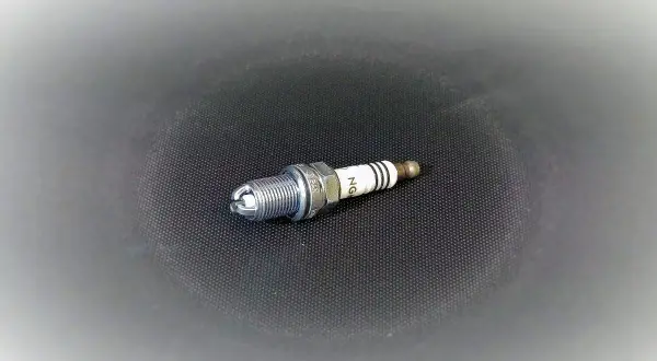 Una bujía lista para el cambio. Su diseño metálico y cerámico blanco con franjas negras indica su función en el motor.