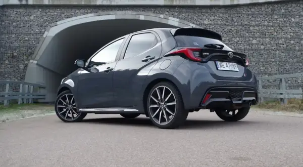 Szary Toyota Yaris Hybrid z czarnym spoilerem i felgami stoi przed tunelem.