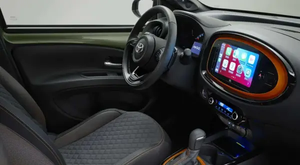 Interni moderni della Toyota Aygo X: sedili trapuntati, volante sportivo e un vivace touchscreen centrale con Apple CarPlay.