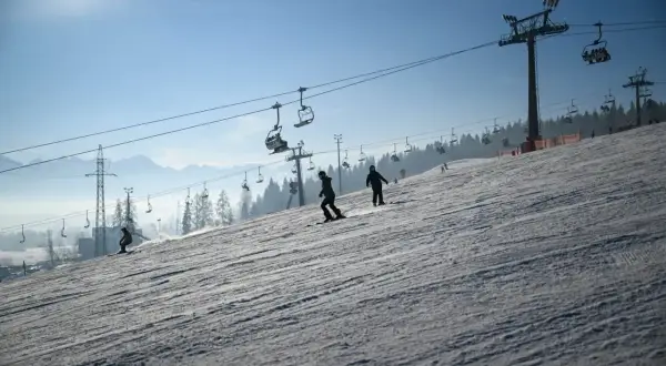 Narciarze i snowboardziści szusują po ośnieżonym stoku, podziwiając piękne widoki. Białka Tatrzańska oferuje wspaniałe atrakcje zimą.