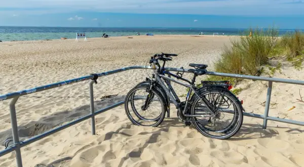 Dwa rowery stojące na piaszczystej plaży, z widokiem na morze i błękitne niebo.