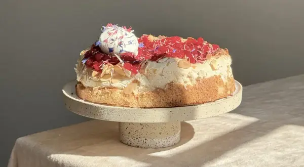 Eine köstliche Sommer Torte mit Baiserhaube, roten Beeren und Mandelsplittern, verziert mit essbaren Blüten.