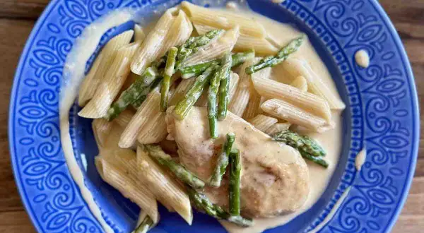 Penne z piersią kurczaka i szparagami w kremowym sosie, podane na niebieskim talerzu.