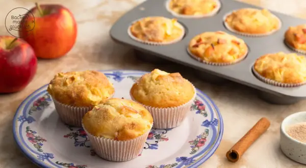 Saftige apfelmuffins ohne zucker, frisch gebacken und auf einem Teller mit Blumenmuster arrangiert. Daneben liegen Äpfel und Zimt.