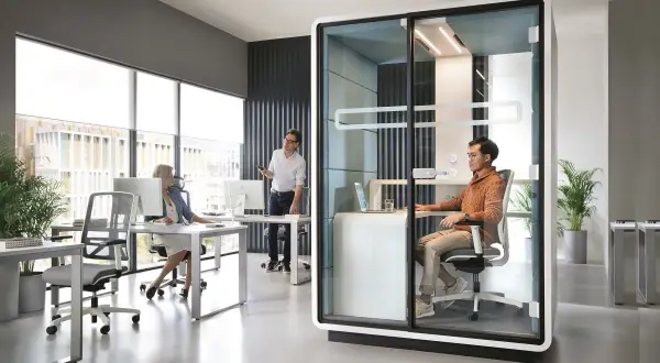 Bureau moderne avec un espace ouvert, une cabine vitrée pour des appels privés et des postes de travail.