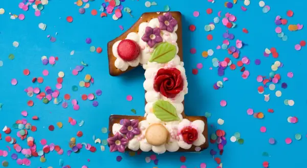 Ein süßer number cake in Form einer Eins, verziert mit Sahne, Blumen und Rosen, umgeben von buntem Konfetti.