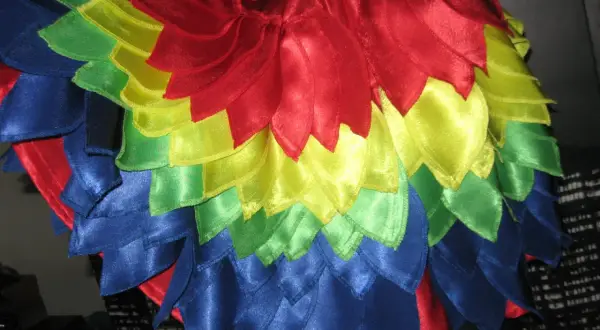 Kolorowy strój papugi dla dziecka, z błyszczącymi piórkami w odcieniach czerwieni, żółci, zieleni i niebieskiego.