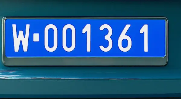 Niebieskie tablice rejestracyjne z numerem W-001361 na ciemnozielonym samochodzie.