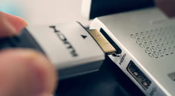 Ein Finger steckt ein HDMI-Kabel in den HDMI-Anschluss eines Laptops.