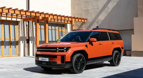 Pomarańczowy, luksusowy SUV Santa Fe stoi przed nowoczesnym budynkiem z drewnianą pergolą.