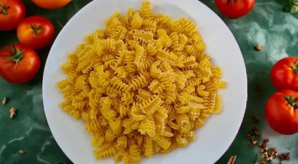 Ein Teller mit gedrehten Nudeln, die aus Hartweizengrieß hergestellt sind, umgeben von frischen Tomaten und Gewürzen.