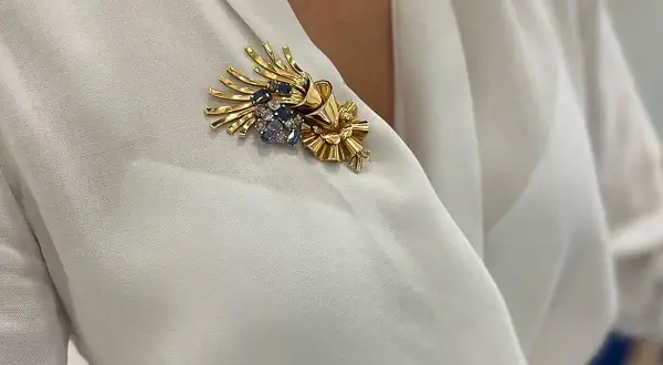 Una joya en forma de broche de oro con zafiros y diamantes, adornando una blusa blanca.