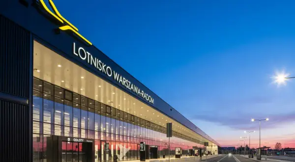 Nowoczesny budynek lotniska Warszawa-Radom z napisem i żółtym logo, o zmierzchu.