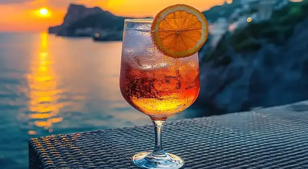Orzeźwiający drink z pomarańczą na tle zachodzącego słońca nad morzem. Idealny na wakacje, zastanawiasz się crodino co to? To włoski aperitif!