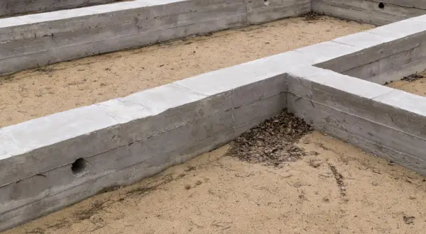 Betonowe fundamenty tworzą zarys przyszłego domu. To stan zero budynku, gdzie piasek miesza się z opadłymi liśćmi.