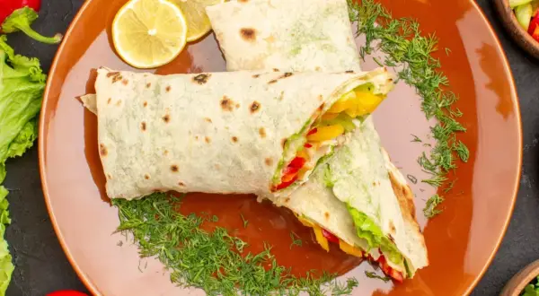Dwa pyszne wrapy z warzywami i kurczakiem, podane na pomarańczowym talerzu z plasterkami cytryny i koperkiem. Idealny fit tortilla na szybki posiłek.