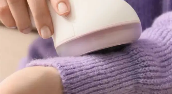Ein Fusselrasierer entfernt lästige Knötchen auf einem lila Pullover.