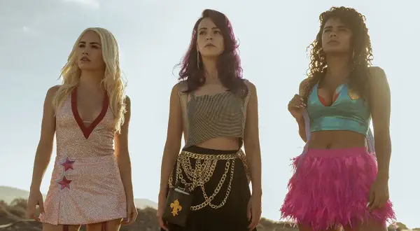 Drei Frauen stehen vor einem hellen, fast roten Himmel. Sie tragen auffällige Outfits.