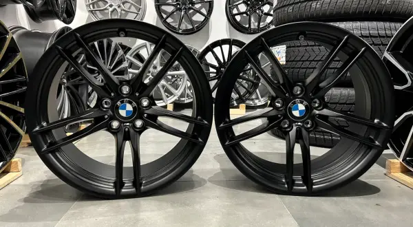 Dwa czarne felgi BMW z logo, idealne do tuningu. W tle inne felgi i opony.