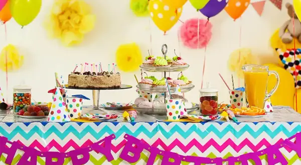 Kolorowy stół z tortem, babeczkami i słodyczami czeka na imieniny Gosi. Balony i girlanda "Happy Birthday" tworzą radosną atmosferę.