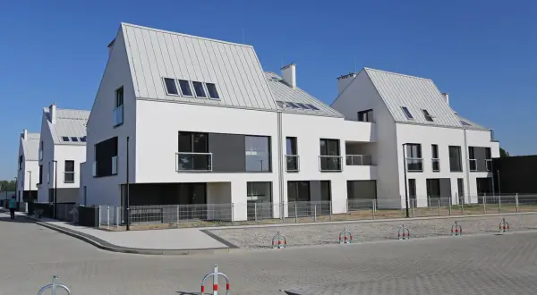 Nowoczesne domy szeregowe z białymi elewacjami i szarymi dachami tworzą malowniczą panoramę osiedla.